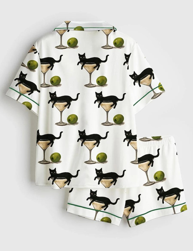 May include: White pyjama set with a repeating pattern of black cats in martini glasses and green olives. The short-sleeved top and shorts have green trim.