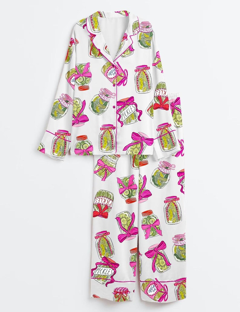 Puede incluir: Conjunto de pijama blanco con un estampado repetido de tarros de pepinillos con lazos rosas y la palabra "Pickles". La parte superior de manga larga y los pantalones tienen ribetes rosas. Los tarros contienen pepinillos verdes.