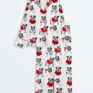 May include: White pyjama set with a repeating pattern of bulldog illustrations. The bulldogs are in black and white, some wearing red sweaters. The set includes a long-sleeved top with red trim and matching trousers.