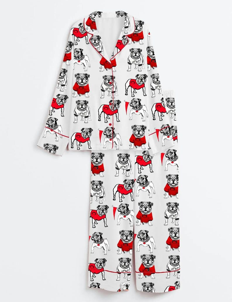May include: White pyjama set with a repeating pattern of bulldog illustrations. The bulldogs are in black and white, some wearing red sweaters. The set includes a long-sleeved top with red trim and matching trousers.