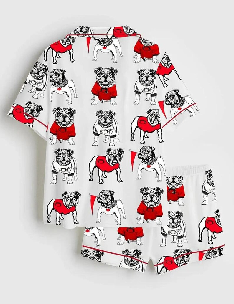 May include: White pyjama set with a repeating pattern of bulldog illustrations. The bulldogs are in black and white, some wearing red sweaters. The set includes a short-sleeved top and matching shorts, both with red trim.