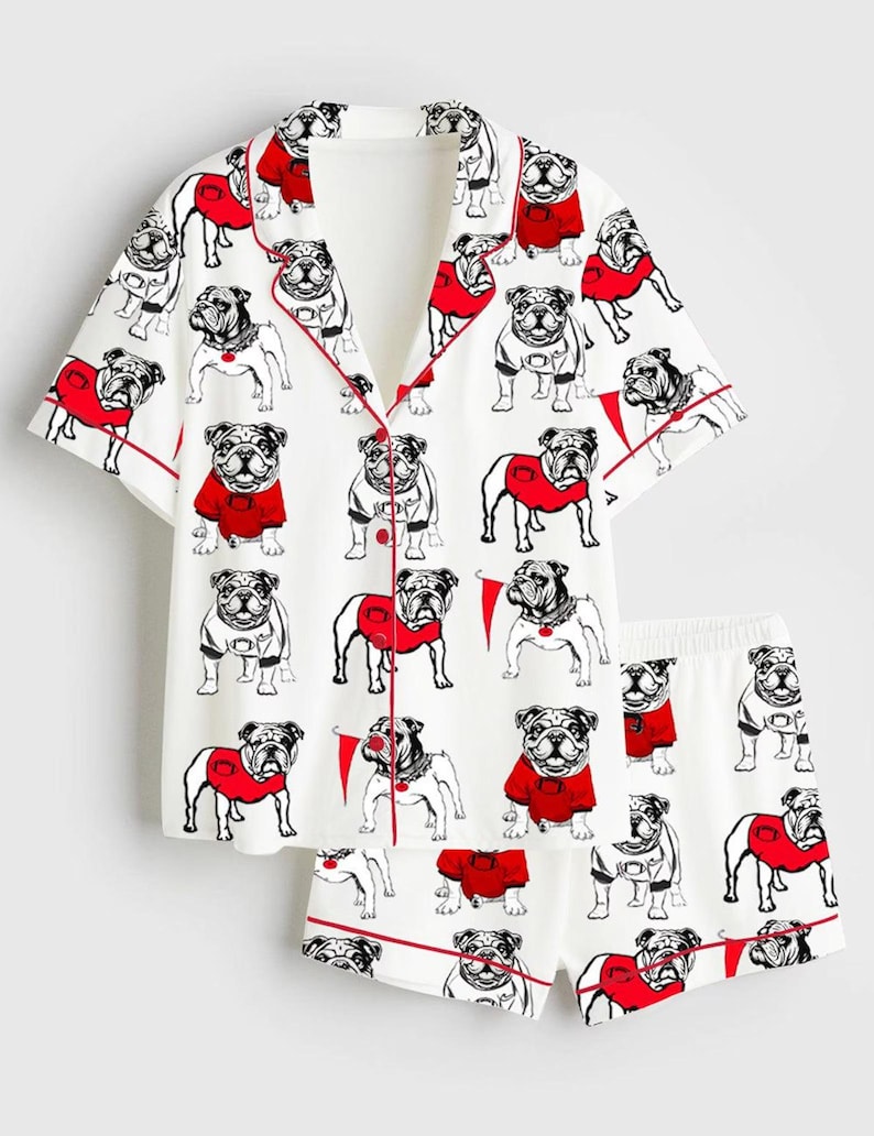 May include: White pyjama set featuring a repeating pattern of bulldog illustrations in red sweaters. The short-sleeved top and shorts have red trim.