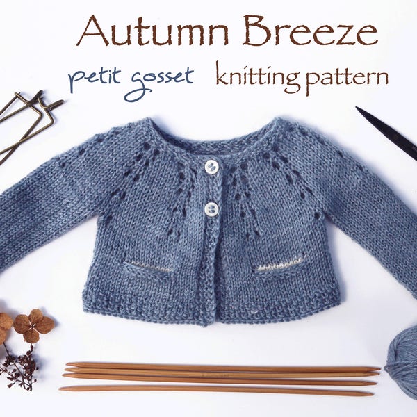 May include: A blue knitted baby cardigan with a button closure and a lace pattern. The cardigan is laid flat on a white surface with knitting needles, yarn, and other craft supplies.