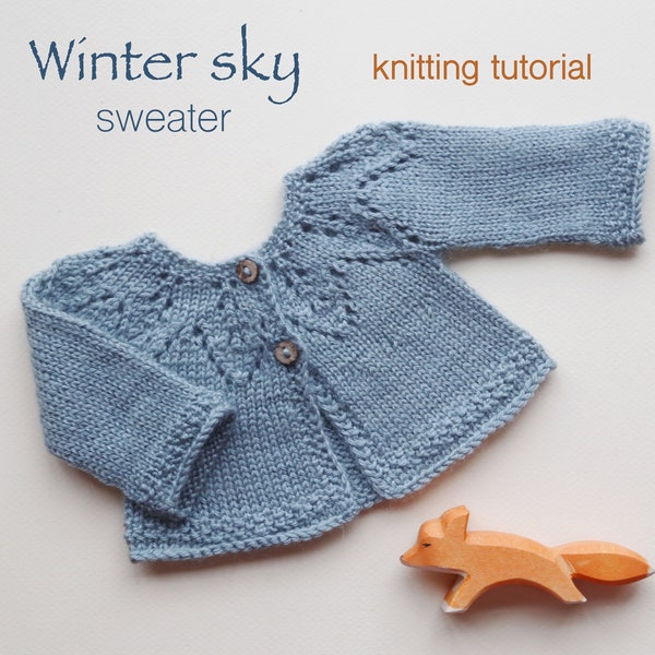 May include: A light blue knitted baby sweater with a button closure and a delicate lace pattern. The sweater is laid flat on a white surface with a wooden fox toy nearby. The text "Winter sky sweater" and "knitting tutorial" is visible above the sweater.