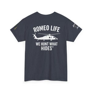 May include: Dark navy blue t-shirt with the text "ROMEO LIFE" above a helicopter graphic and the phrase "WE HUNT WHAT HIDES". The shirt also has a small graphic on the left sleeve and text on the right sleeve.