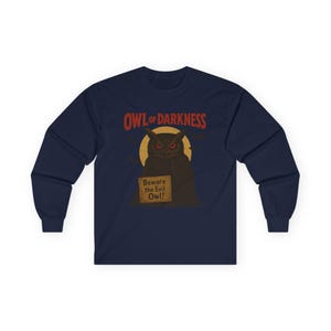 以下が含まれることがあります： 赤い目をした暗いフクロウ、黄色い月、そして「OWL OF DARKNESS」の文字が描かれたネイビーブルーの長袖シャツ。フクロウは「Beware the Evil Owl!」と書かれた看板を持っています。