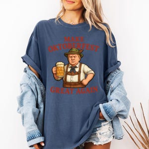 May include: Navy blue t-shirt with the text "MAKE OKTOBERFEST GREAT AGAIN" in red. The graphic features a cartoon of a man in traditional Bavarian attire holding a beer stein. The shirt is a casual, oversized fit.