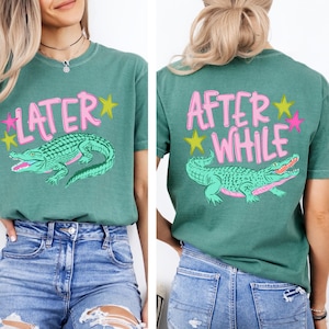 May include: Green t-shirt with a pink and yellow design. The front of the shirt says "LATER" with a green alligator graphic. The back of the shirt says "AFTER WHILE" with a matching alligator graphic.