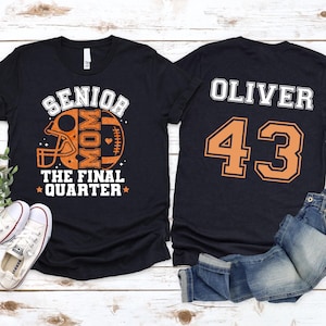 May include: A black t-shirt featuring a front graphic of a football helmet and ball with the text SENIOR MOM THE FINAL QUARTER in orange and white. The back of the shirt displays the name OLIVER and the number 43 in large orange and white text.