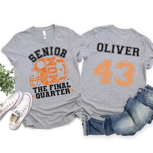 May include: Two heather gray t-shirts. The front features an orange football helmet graphic with the text SENIOR MOM THE FINAL QUARTER. The back displays the name OLIVER and the number 43 in black and orange block lettering.