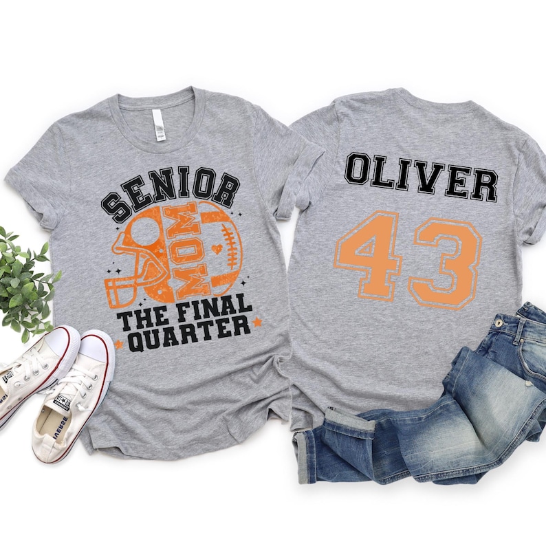 May include: Two heather gray t-shirts. The front features an orange football helmet graphic with the text SENIOR MOM THE FINAL QUARTER. The back displays the name OLIVER and the number 43 in black and orange block lettering.