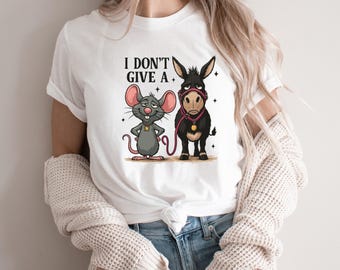 May include: White t-shirt featuring a cartoon illustration of a gray mouse and a black donkey with the text "I DON'T GIVE A." The mouse has a yellow star on its chest. The donkey wears a pink halter.
