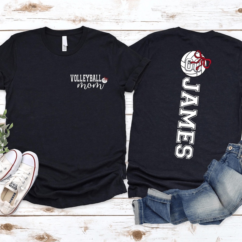 May include: Black t-shirts with white text and volleyball graphics. One shirt says "Volleyball Mom" with a volleyball and bow graphic. The other shirt has the name "JAMES" vertically with a volleyball and bow graphic.
