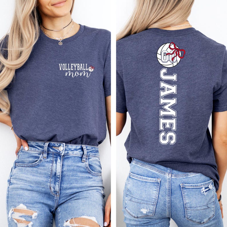 May include: A navy blue t-shirt with the words "Volleyball Mom" in white script on the front. The back of the shirt features a volleyball graphic with a red bow and the name "JAMES" in white block letters.