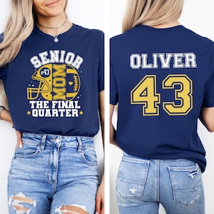 May include: A navy blue t-shirt featuring a front graphic with a yellow football helmet, the text SENIOR MOM THE FINAL QUARTER, and #43. The back of the shirt displays the name OLIVER in white and the number 43 in yellow with a white outline.