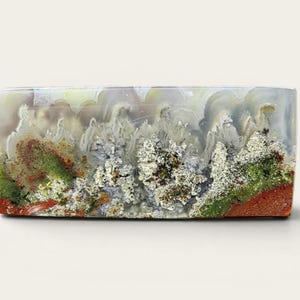 Op de afbeelding: Een rechthoekig decoratief object met een natuurstenen uitstraling. De steen heeft een mix van kleuren, waaronder wit, grijs, groen, rood en bruin, waardoor een uniek, organisch patroon ontstaat. Het object heeft een gepolijst, glad oppervlak.