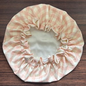 May include: A pink and white gingham shower cap with a ruffled edge. The cap has a satin lining and a drawstring closure. The cap is designed to protect hair from water while showering.