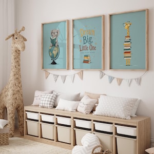 Könnte beinhalten: Drei gerahmte Kunstdrucke mit Tierillustrationen und dem Text "Dream Big, Little One". Die Drucke zeigen einen Elefanten, eine Giraffe und einen Stapel Bücher. Eine gewebte Giraffenstatue und eine Aufbewahrungsbank mit weißen Behältern befinden sich ebenfalls im Raum.