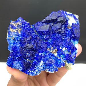 May include: A vibrant blue lapis lazuli specimen with crystalline structures and flecks of gold pyrite. The natural stone displays a rich, deep blue color with a rough, textured surface. This mineral specimen is a beautiful example of natural lapis lazuli.