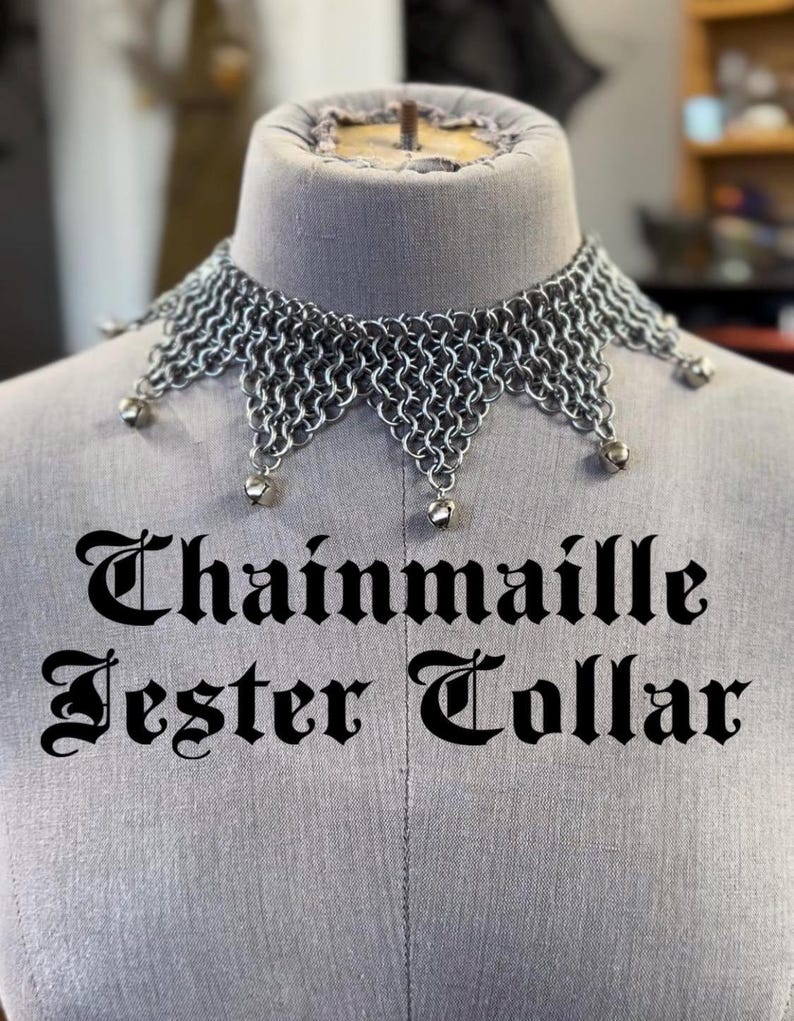 Puede incluir: Collar de buf&oacute;n de cota de malla plateada, exhibido en un maniqu&iacute;. El collar tiene un borde festoneado y peque&ntilde;as campanas colgantes. El texto "Chainmail Jester Collar" est&aacute; impreso en negro, con fuente g&oacute;tica.