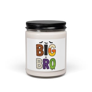 Pode incluir: Um frasco de vela de vidro com tampa preta e um rótulo branco com o texto BIG BRO em letras coloridas com temas de Halloween. As letras incluem listras laranja e pretas, pontos brancos, milho doce e texturas de lodo na cor verde.