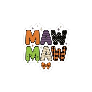 May include: A die-cut sticker featuring the text MAW MAW in two rows. The letters have various patterns including orange grid, purple stripes, black stars, green slime, mummy bandages, and orange diamonds, accented by small stars and an orange bow.