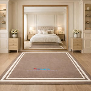 May include: A large, rectangular brown rug with a white border and a double white stripe. The rug is in a bedroom with a large mirror, a bed, and two nightstands. The room has a neutral color palette.