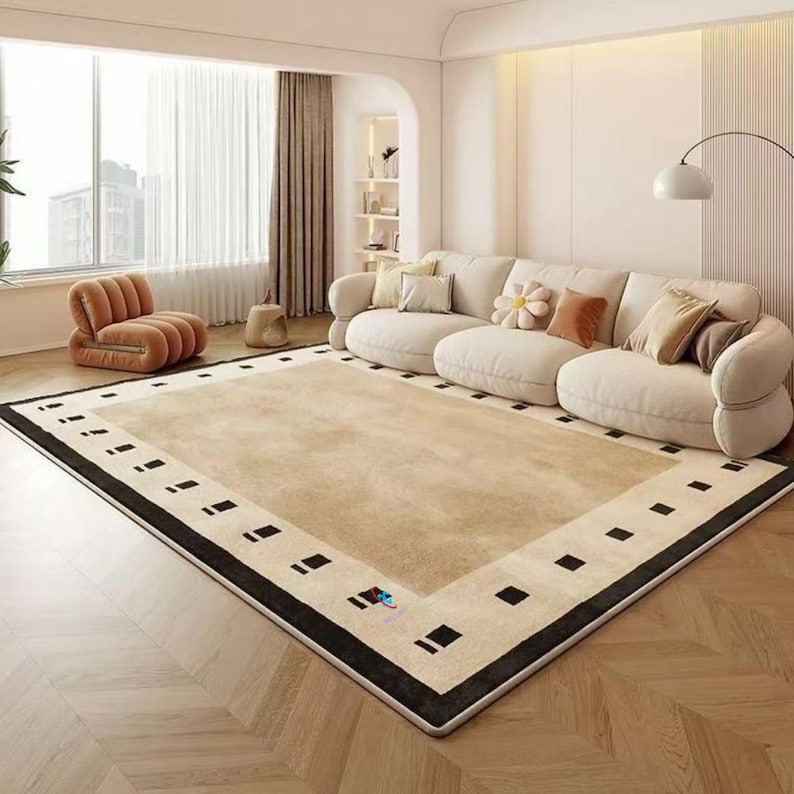 Pode incluir: Um grande tapete bege com borda preta e padr&otilde;es geom&eacute;tricos. O tapete est&aacute; numa sala de estar com um sof&aacute; creme, uma poltrona p&ecirc;ssego e uma grande janela com cortinas. Mede aproximadamente 300 cm x 200 cm.