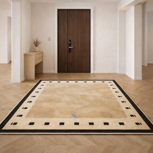 Pode incluir: Um tapete retangular bege com uma borda preta e detalhes quadrados. O tapete est&aacute; colocado sobre um ch&atilde;o de madeira em um quarto bem iluminado, com uma porta marrom escura ao fundo. O design do tapete adiciona um toque de eleg&acirc;ncia ao espa&ccedil;o.