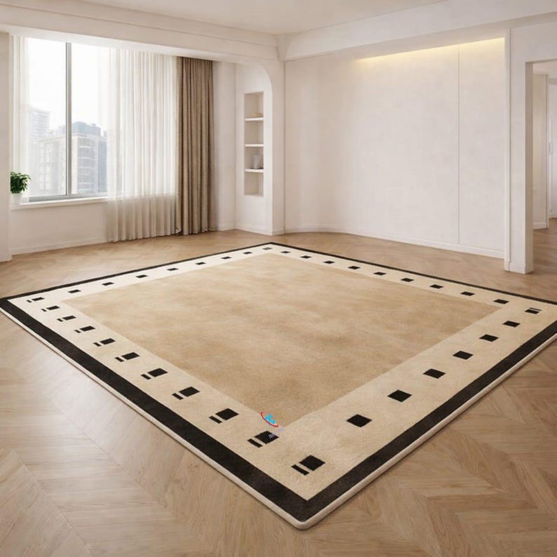 Pode incluir: Um tapete bege retangular grande com uma borda preta e um padr&atilde;o repetitivo de quadrados pretos. O tapete est&aacute; centrado em uma sala com piso de madeira e uma grande janela.