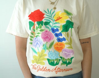 May include: A white t-shirt with a colorful floral design and the text "The Golden Afternoon".