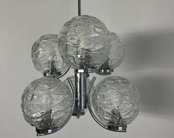 Puede incluir: Una lámpara de araña vintage con cinco globos de vidrio texturizado. Los globos están dispuestos alrededor de un accesorio central cromado. La lámpara cuelga de una sola varilla cromada. Los globos de vidrio tienen una superficie estampada única.