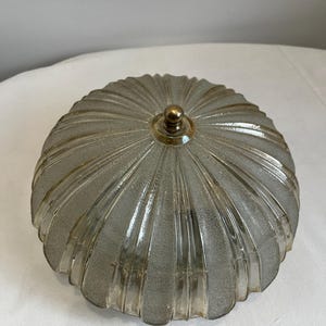 May include: A vintage, frosted glass light fitting with a ribbed, rounded design. The fitting has a brass-coloured finial on top. The glass has a textured, speckled appearance. The overall shape is reminiscent of a shell.