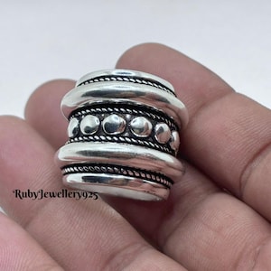 Puede incluir: Un anillo ancho, plateado con un diseño texturizado. El anillo presenta múltiples bandas con una textura de cuerda y una fila de pequeños adornos redondos. El texto "RubyJewellery925" es visible.