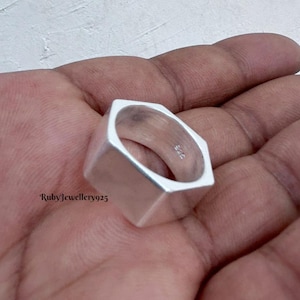 Könnte beinhalten: Ein silberner Ring mit sechseckiger Außenform und kreisförmigem Innenband. Die Innenseite des Rings ist mit dem Text 925 gestempelt, was auf eine Zusammensetzung aus Sterlingsilber hinweist. Die Oberfläche ist glatt, poliert und metallisch.