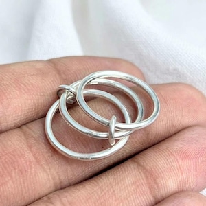 May include: A set of three interlocking silver rings with a smooth, polished finish. The rings are connected to form a single unit, featuring a simple, rounded band design that creates a continuous, fluid shape when linked together.