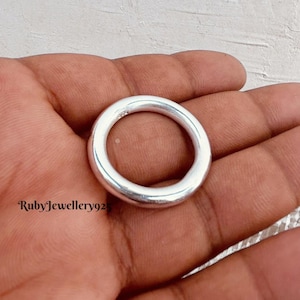 May include: A plain silver ring with a smooth, rounded design. The ring is circular and made of polished metal. The ring is held in a hand, and the text "RubyJewellery925" is visible.