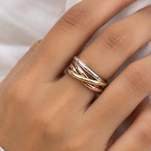 May include: A tri-colour ring featuring three interlocking bands in polished silver, yellow gold, and rose gold tones. The smooth, rounded metal bands are intertwined to create a continuous, layered design that sits comfortably on the finger.