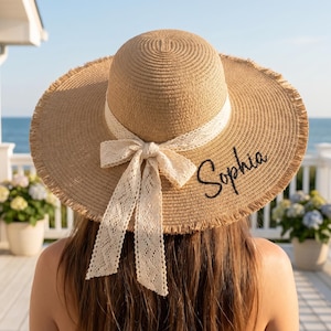 Peut inclure: Chapeau de paille à larges bords, orné d'un ruban et d'un nœud en dentelle crème. Le chapeau porte le nom "Sophia" brodé en écriture noire. Conçu pour la protection solaire, il est idéal pour les activités en plein air.
