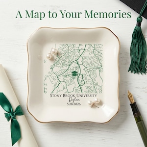 May include: Cream ceramic trinket dish with a gold rim, featuring a green map design of Stony Brook University. The dish includes the text "A Map to Your Memories", the university name, a name, and a date. Two pearl earrings are placed on the dish.
