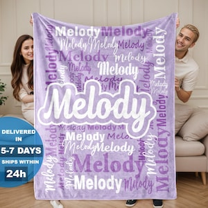 May include: A lavender blanket with the name "Melody" in a large, white, stylized font. The name is repeated in various sizes and orientations across the blanket. The blanket is held up by two people.