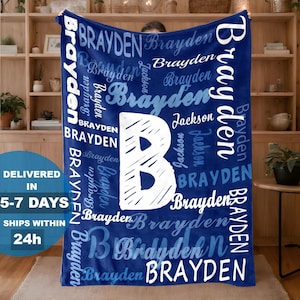 May include: A navy blue blanket with the name "Brayden" in white script and block letters. A large white "B" is centered on the blanket. The blanket is displayed in front of a wooden bookshelf.