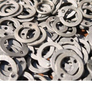 May include: A close-up shot of a pile of silver-colored retaining rings. The rings are circular with a split and two holes. The image is well-lit, showing the details of the metal. The rings are likely used in mechanical or engineering applications.