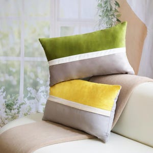 May include: Two rectangular decorative pillows. One is green and gray with a white stripe, the other is yellow and gray with a white stripe. The pillows are on a white couch with a beige throw.