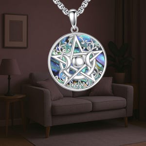 Puede incluir: Collar con colgante de plata con un diseño de pentagrama y una incrustación de nácar. El colgante tiene un diseño calado con detalles de luna creciente. El collar se muestra sobre un fondo de habitación.