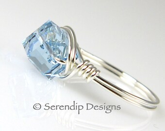 May include: A silver ring with a light blue square-shaped gemstone wrapped in silver wire. The ring is on a white background.