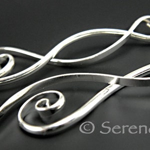 Puede incluir: Un par de pendientes de plata con un diseño abstracto en espiral. Los pendientes están hechos de alambre fino y retorcido y tienen un aspecto delicado y femenino.