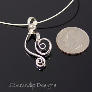 May include: A silver-colored pendant in the shape of a treble clef, with a spiral design. The pendant is on a thin, silver-colored necklace. A U.S. dime is next to the pendant for size comparison. The pendant is on a black surface.
