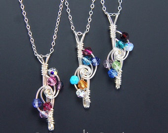 May include: Three silver necklaces with a treble clef pendant adorned with colorful crystals. Each pendant features a different color scheme, including turquoise, purple, and green.