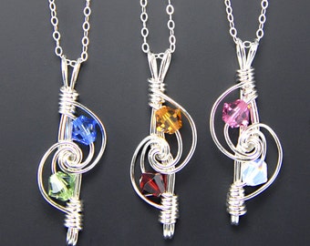 May include: Three silver necklaces with treble clef pendants adorned with colorful crystals. Each pendant features a different combination of blue, green, red, orange, and pink crystals.